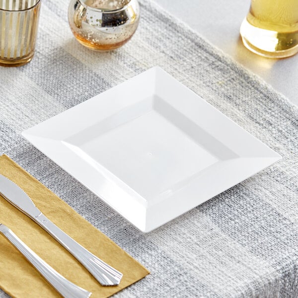 A white square Visions plastic plate with a knife and fork on it on a table.