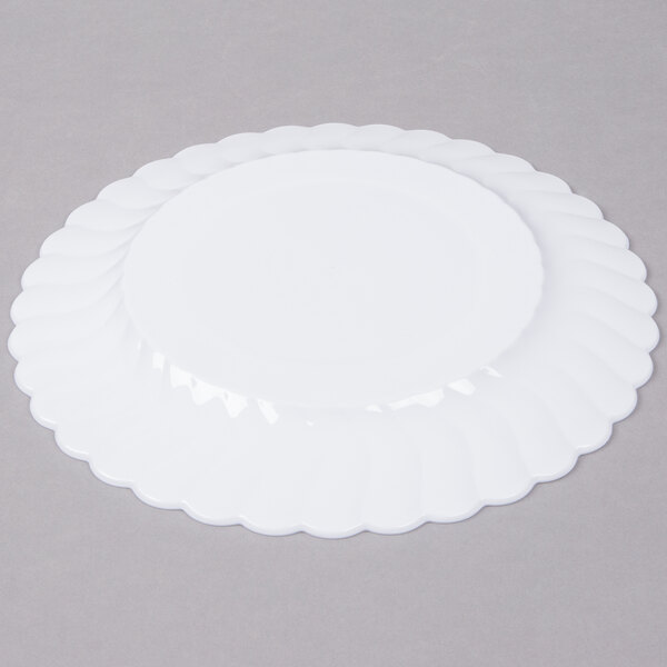 A white Fineline Flairware plastic plate with scalloped edges on a white surface.