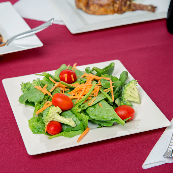 A Visions Florence ivory plastic plate with salad, broccoli, and tomatoes on a table.
