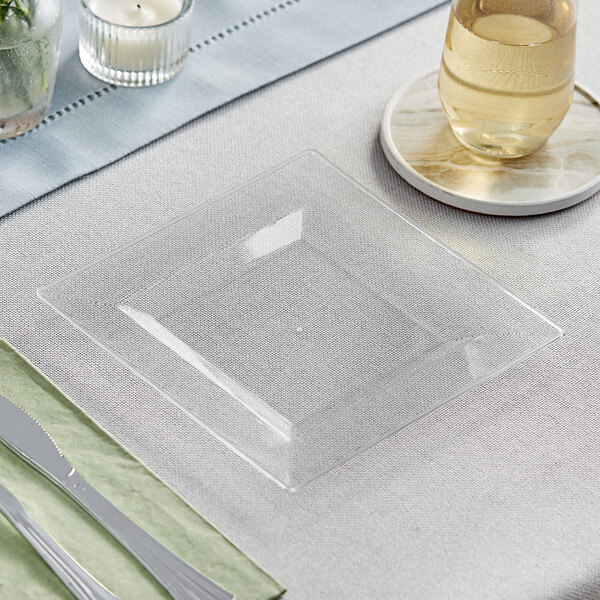 A Visions Florence clear square plastic plate with a knife and fork on a table.