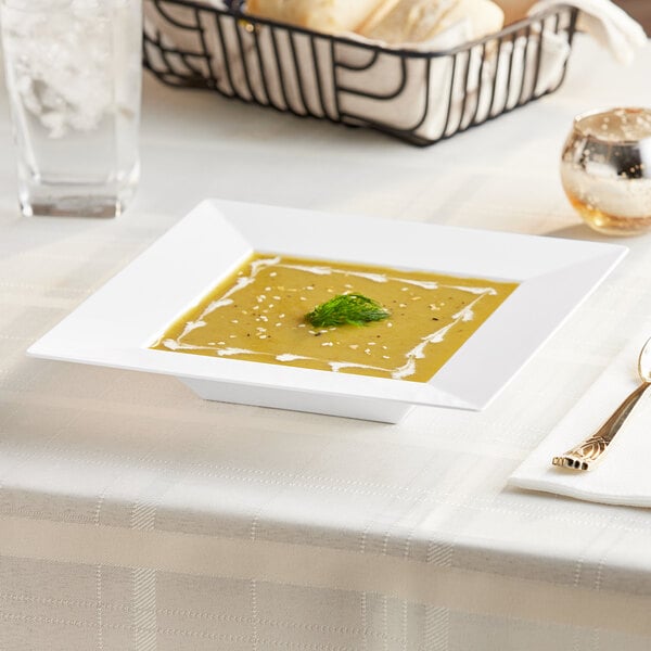 A Visions white square plastic bowl filled with soup on a table.