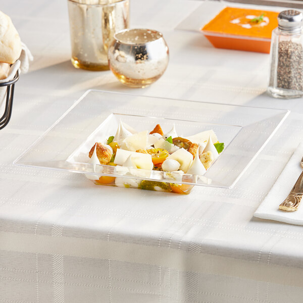 A clear square plastic bowl filled with soup on a table.