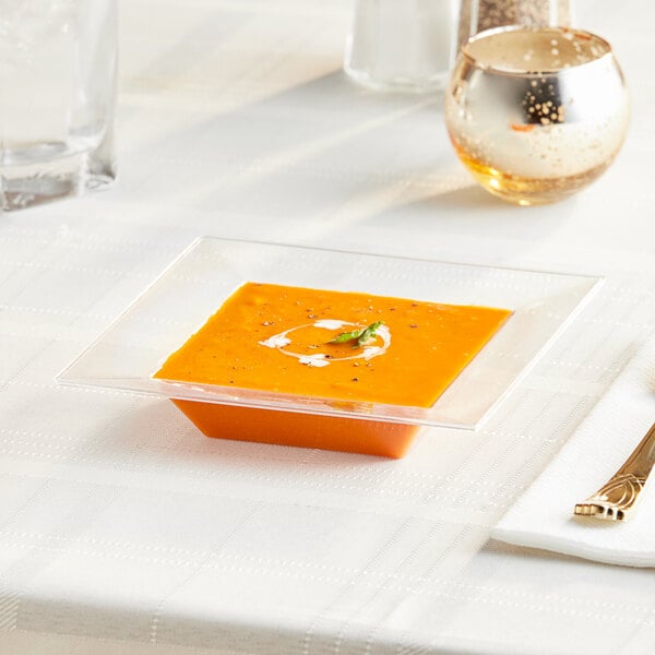 A Visions Florence clear square plastic bowl filled with soup on a table.