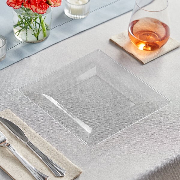 A Visions clear square plastic plate with silverware on a table.