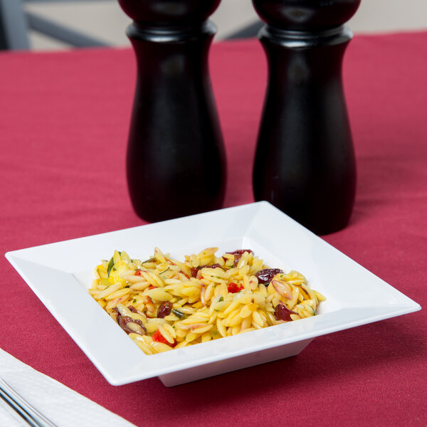 A Visions white square plastic bowl filled with food on a table.