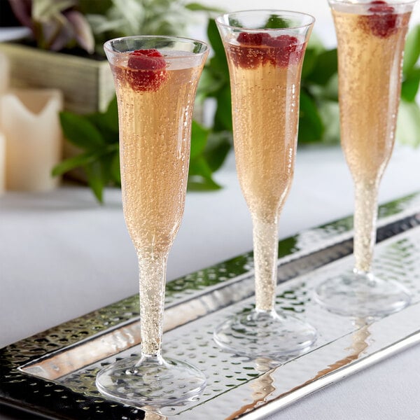 A set of clear plastic champagne flutes filled with sparkling beverage and garnished with raspberries, displayed on a tray.