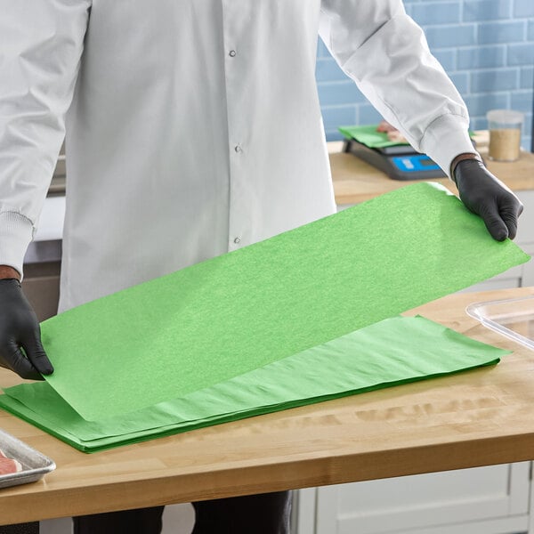 A stack of green steak paper sheets being handled by a person wearing gloves and a white coat.
