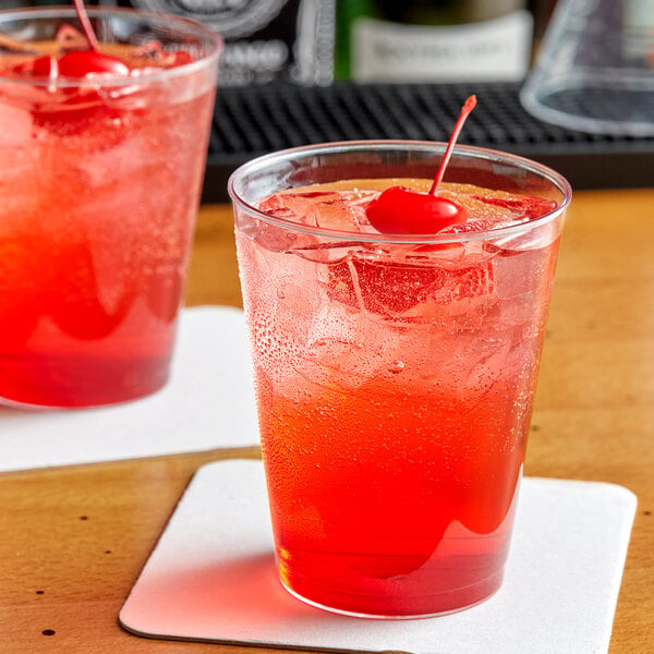 Two Choice clear plastic tumblers filled with red liquid and cherries on a table in a cocktail bar.