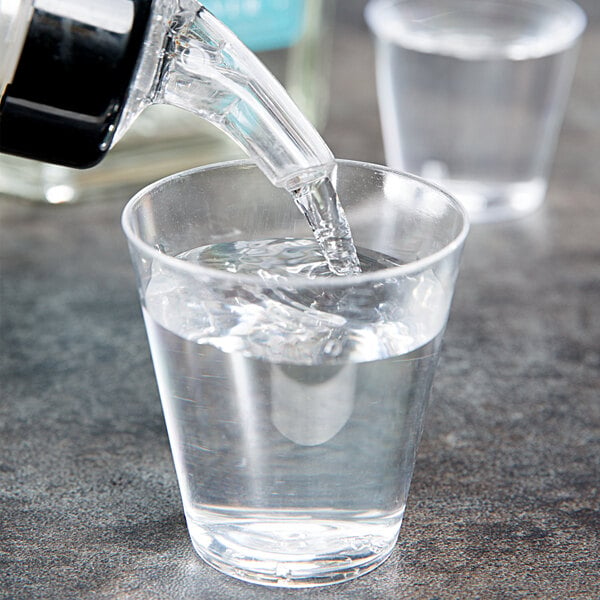 A person pouring water from a water filter into a Choice clear plastic shot glass.