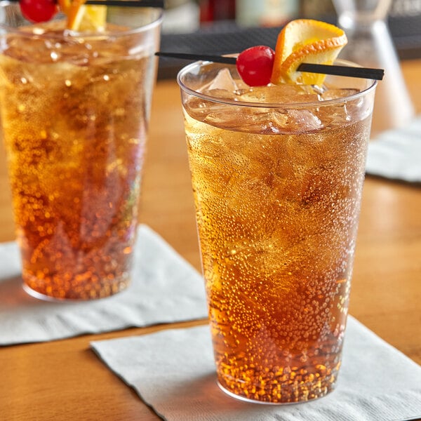 Two Choice clear plastic tumblers filled with brown liquid, ice, and fruit slices.