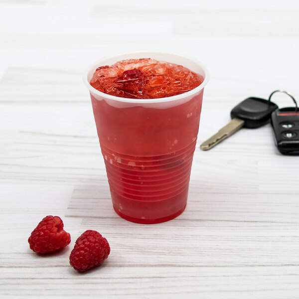 A Dart translucent plastic cup filled with red liquid, ice, and raspberries with a key next to it.