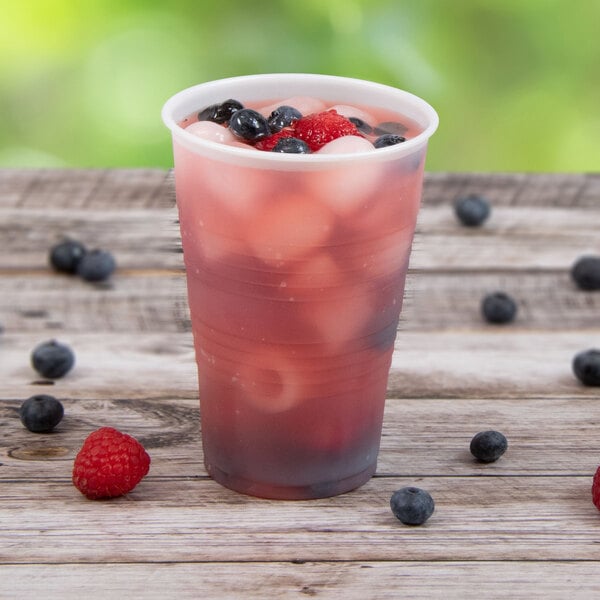 A Dart Conex translucent plastic cup filled with berries and ice on a wooden table.