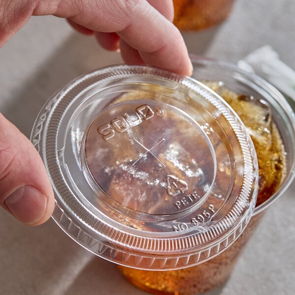 A clear plastic Solo lid with a straw slot being placed on a beverage cup.