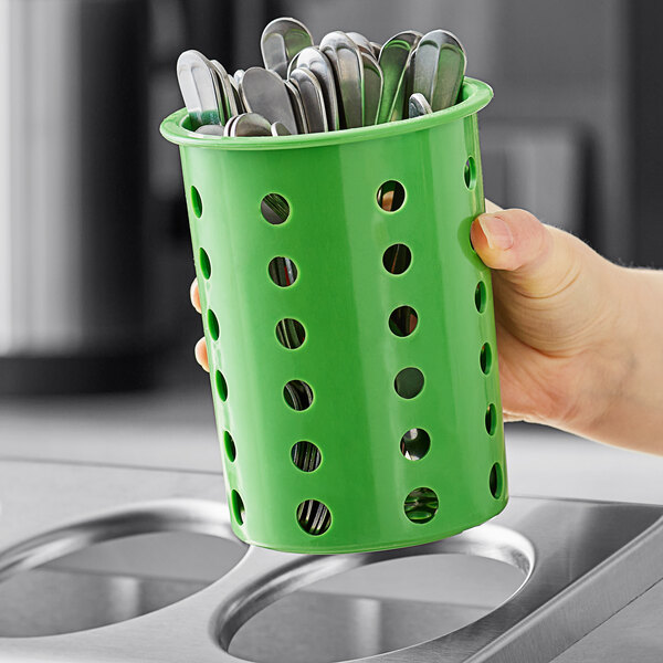 A hand holding a green Steril-Sil flatware cylinder with spoons inside.