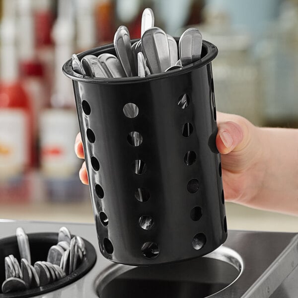 A hand holding a black Steril-Sil flatware cylinder with silverware inside.