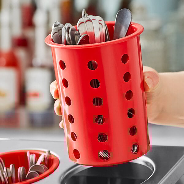 A hand holding a red Steril-Sil plastic flatware cylinder with silverware in it.
