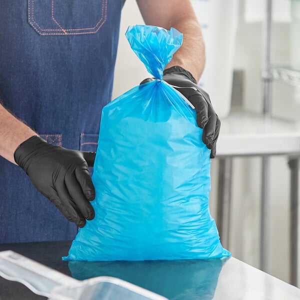 A blue heavy duty plastic ice bag being held by a person wearing black gloves.