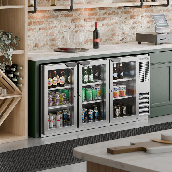 A stainless steel underbar height back bar refrigerator with three glass doors, stocked with various beverages.