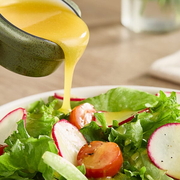 A bowl of salad with Monin Passion Fruit Puree being poured over it.