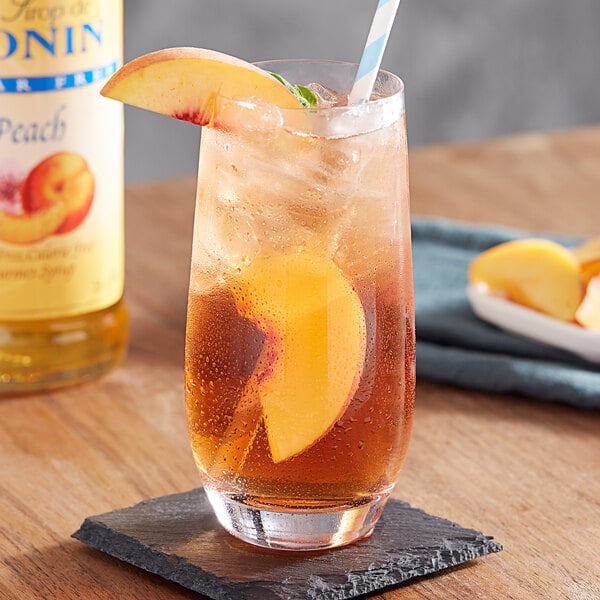 A glass of iced peach tea with a straw and a peach slice.