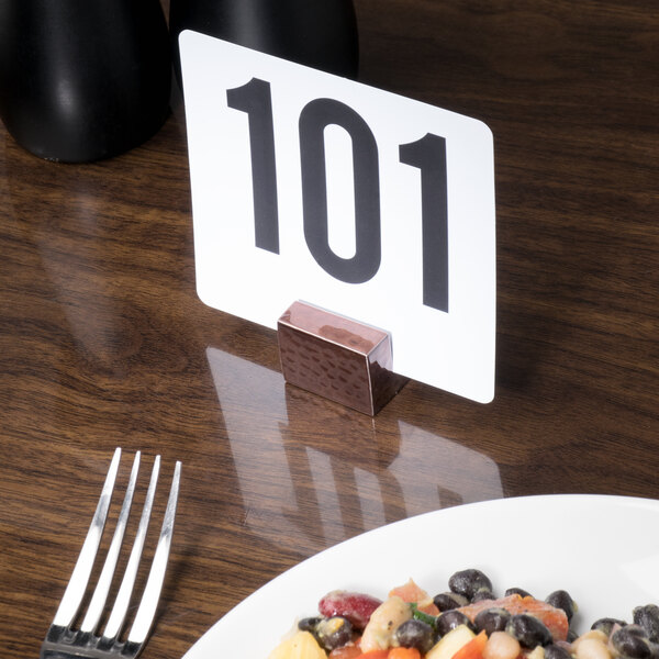 An American Metalcraft rectangular hammered copper table card holder on a wood table with a plate of food.