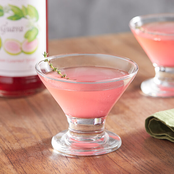 A glass of Monin guava cocktail garnished with a sprig of thyme.