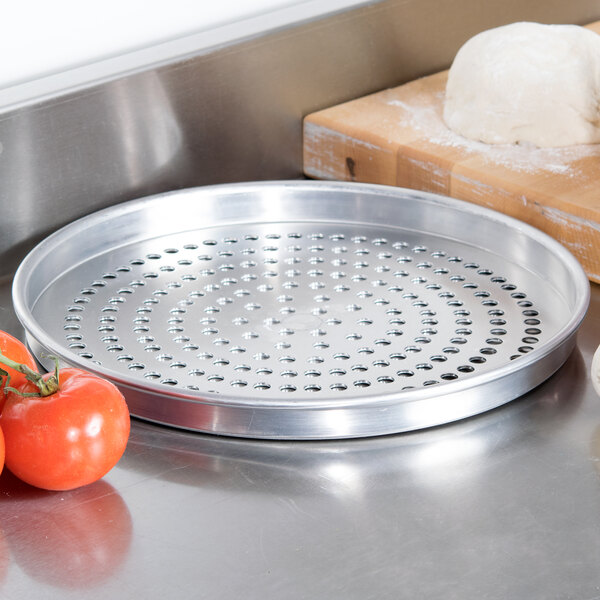 An American Metalcraft straight-sided pizza pan with a ball of dough and tomatoes on it.