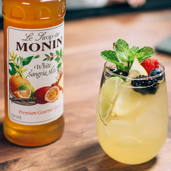 A white bottle of Monin Premium White Sangria Mix next to a glass of sangria with fruit.