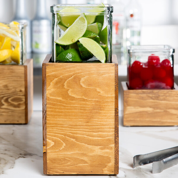 A Cal-Mil rustic pine riser with 3 glass jars filled with limes.