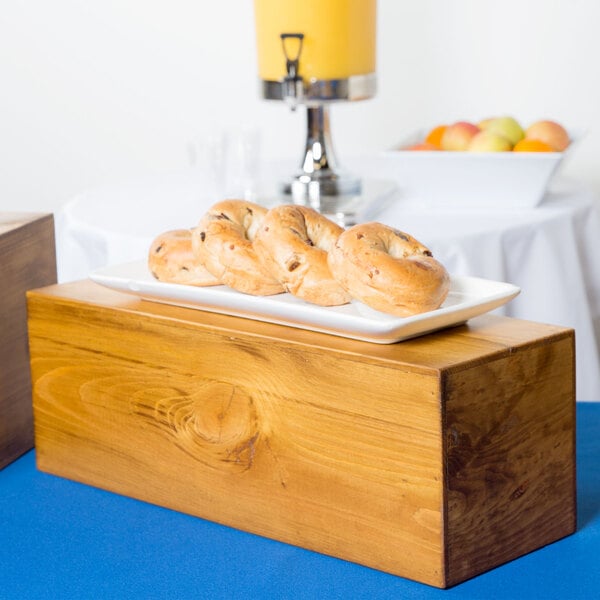 A Cal-Mil Madera rustic pine rectangle plate riser holding a plate of bagels on a table.