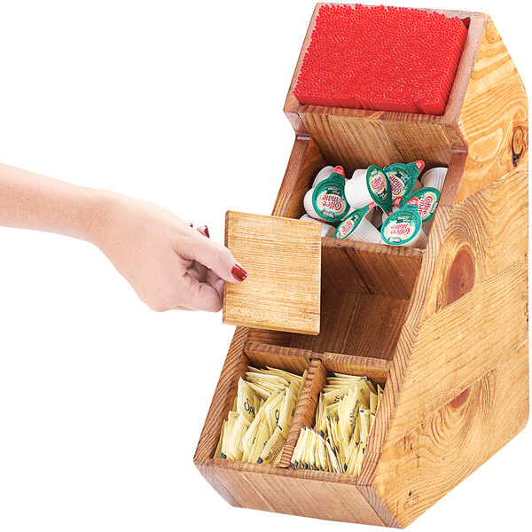 A hand holding a Cal-Mil Madera rustic pine condiment display with stir sticks in it.