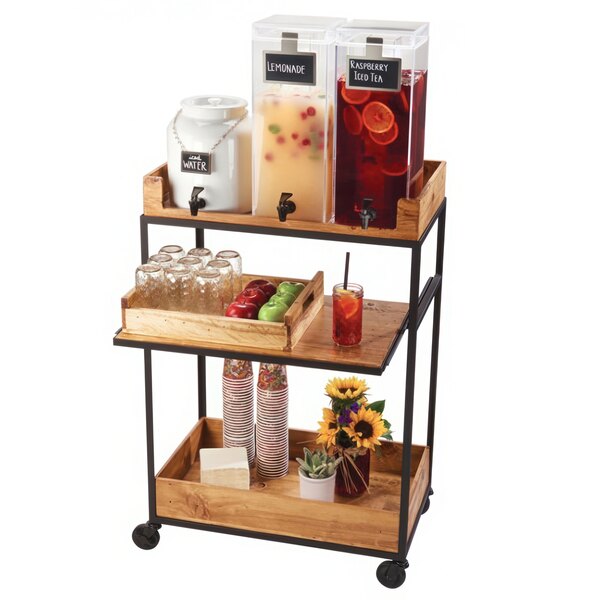 A Cal-Mil clear acrylic beverage dispenser with ice in it on a wooden cart with drinks and fruit.