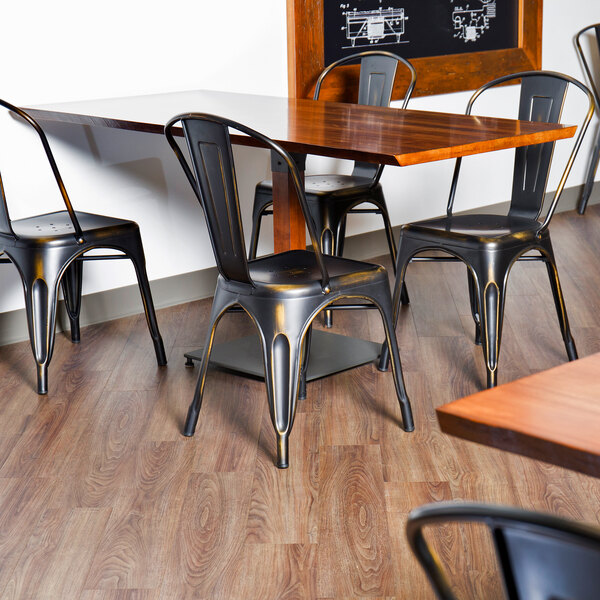 A black Flash Furniture distressed copper metal chair with wood and metal legs next to a wood table in a restaurant dining area.