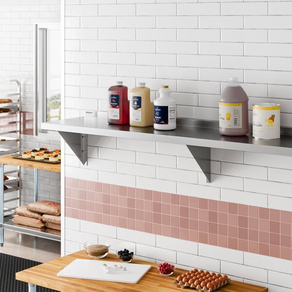 A heavy-duty stainless steel wall shelf mounted on a tiled kitchen wall, holding various large containers.