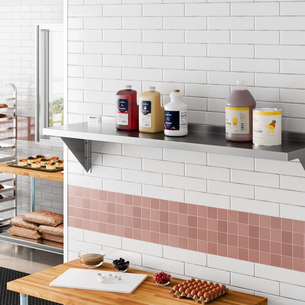 A stainless steel heavy-duty wall shelf mounted on a tiled kitchen wall, holding various large containers.