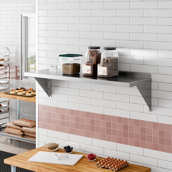 A stainless steel wall-mounted shelf holding containers of ingredients in a commercial kitchen setting.