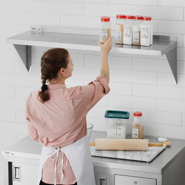 A woman in a pink shirt standing on a Regency stainless steel wall shelf holding a container of spices.