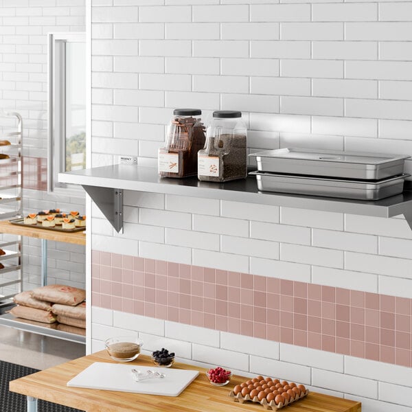 A stainless steel wall-mounted shelf with containers and trays placed on it, installed in a commercial kitchen setting.