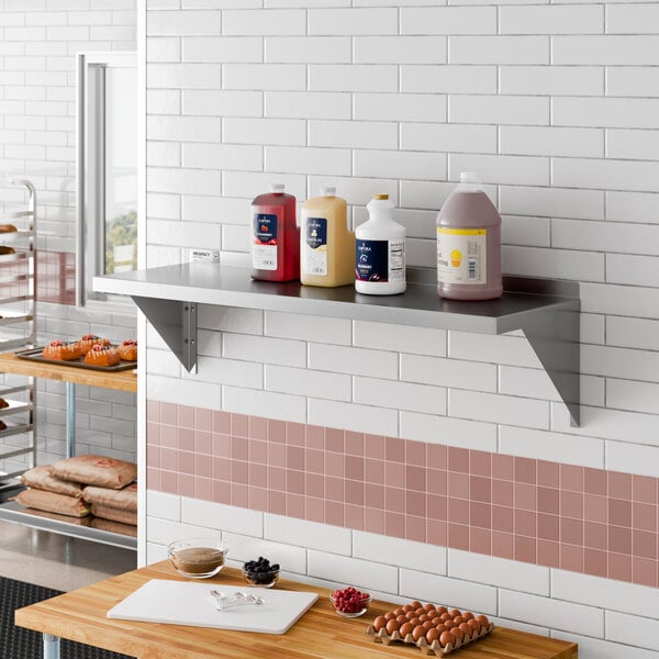 A stainless steel heavy-duty wall shelf mounted on a tiled kitchen wall.