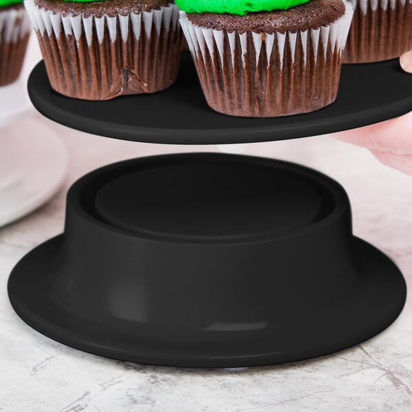 A person holding a tray of cupcakes on a black Elite Global Solutions round pedestal.