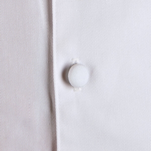 A close up of a Chef Revival white long sleeve chef coat with a button.
