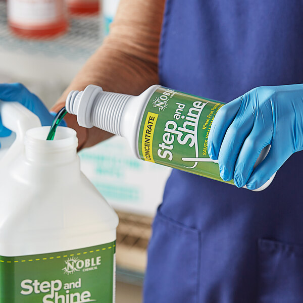 A person in blue gloves pouring Noble Chemical Step and Shine floor cleaner from a white bottle into a green container.