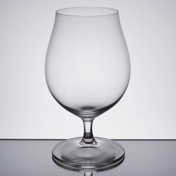 A Spiegelau stemmed pilsner glass filled with beer on a reflective surface.