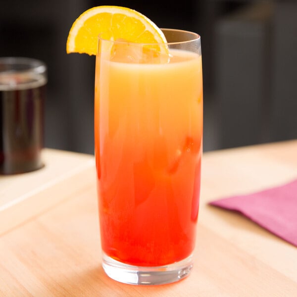 A Spiegelau Soiree highball glass filled with orange liquid and a slice of orange on the rim.