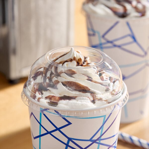 A clear plastic dome lid with a 2-inch hole, fitted on a paper cup filled with a whipped cream and chocolate-topped beverage.
