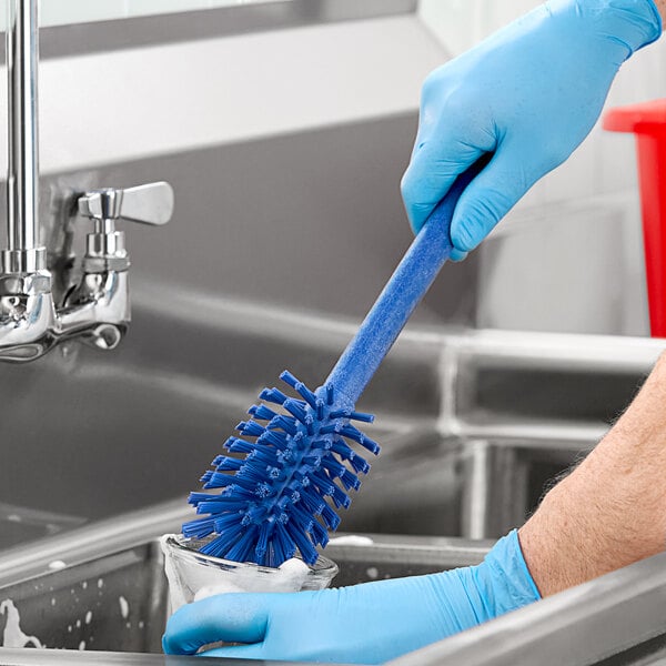 A person in blue gloves using a Carlisle blue bottle cleaning brush to clean a sink.