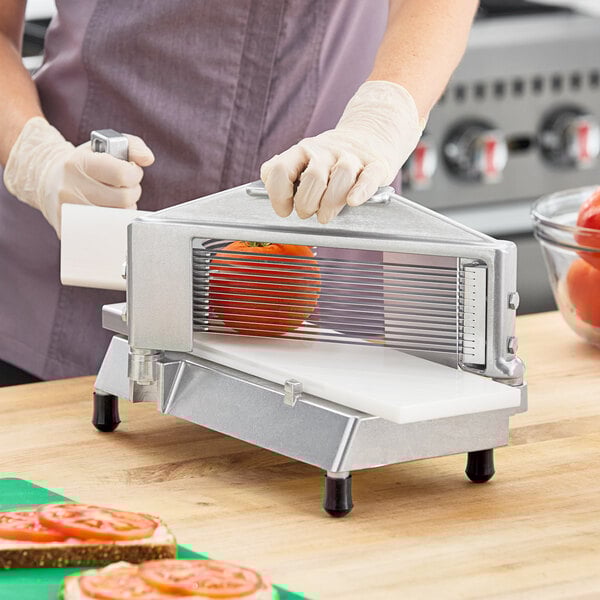 A commercial tomato slicer with a metal frame and multiple blades, designed for quickly slicing tomatoes.