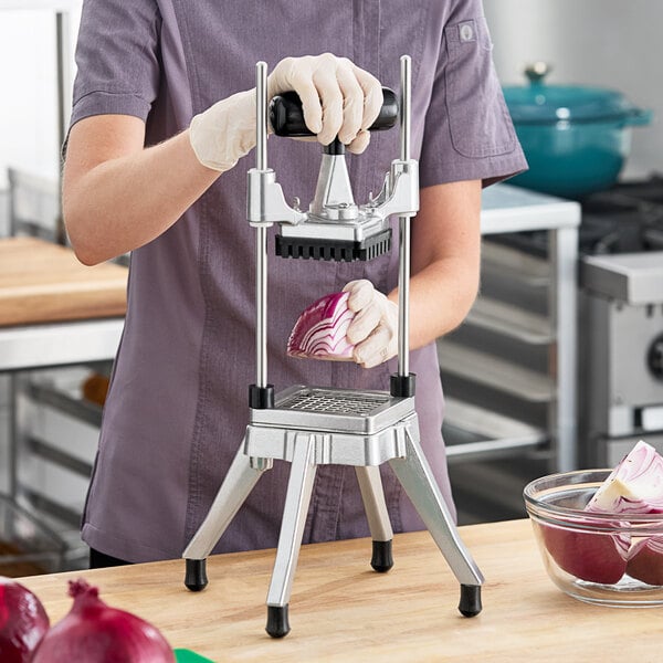 A metal vegetable dicer with a lever handle being used to dice a red onion.