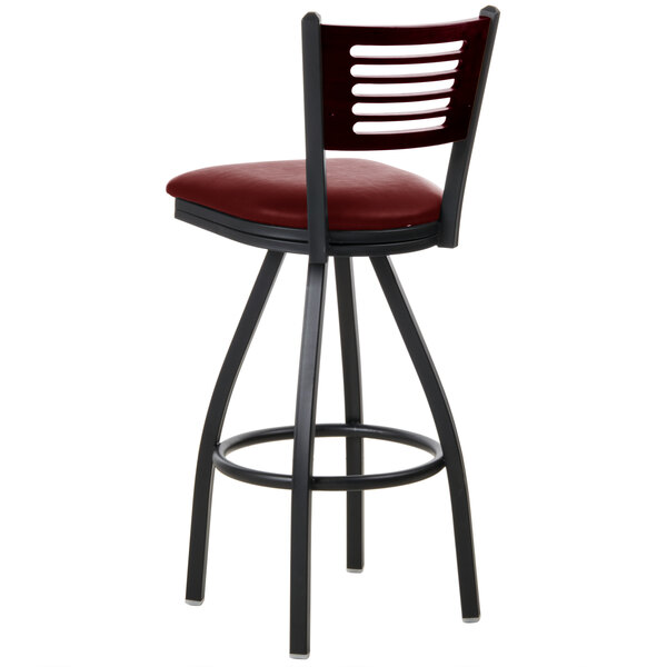 A BFM Seating black metal bar stool with a mahogany wood back and red vinyl seat.