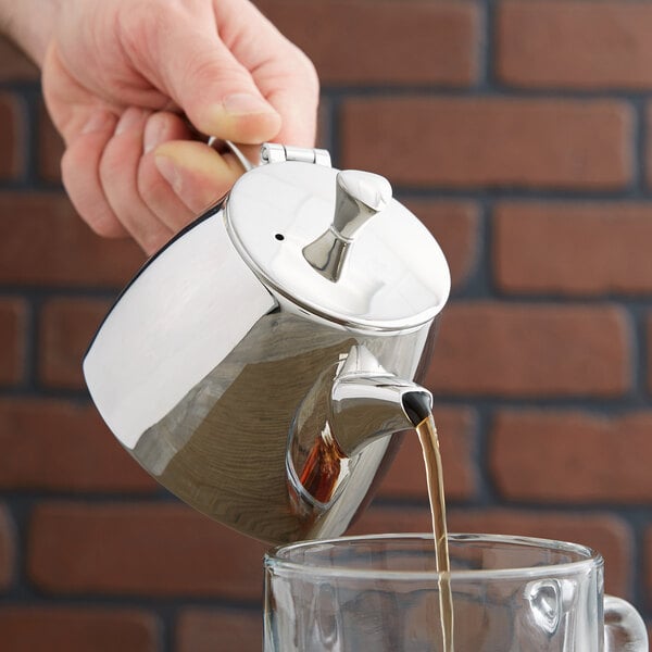 A hand pouring liquid into a Vollrath stainless steel teapot.